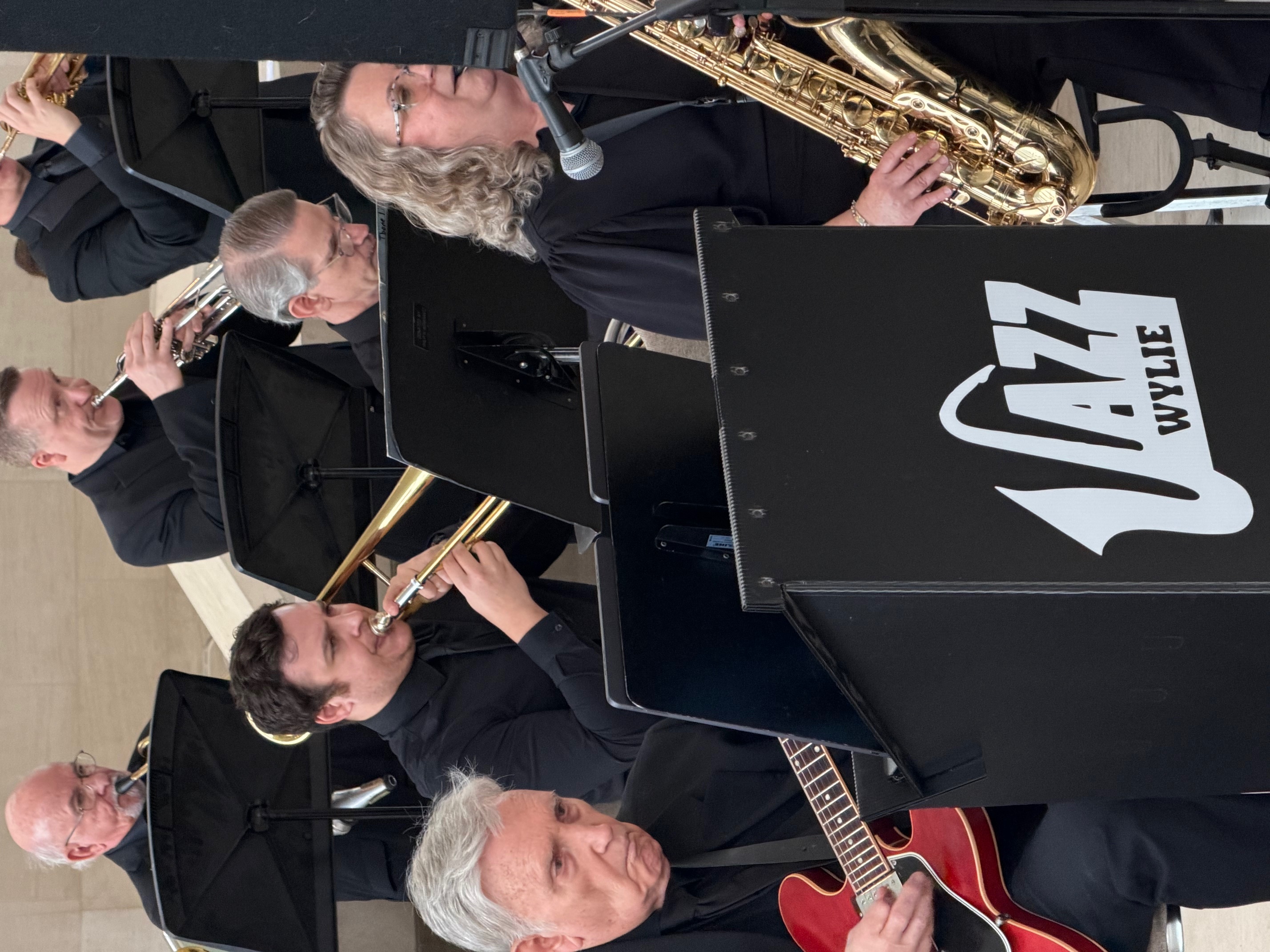 Jazz Wylie community band performing, with trombone, trumpet, guitar, saxophone and other musicians in black attire